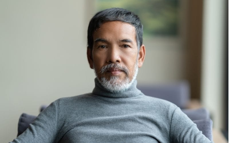 Older man with a grey beard has a popular asian man hairstyle and wears an elegant turtleneck