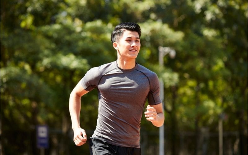 Attractive asian man smiles as he runs and his hairstyle is perfect while outdoors