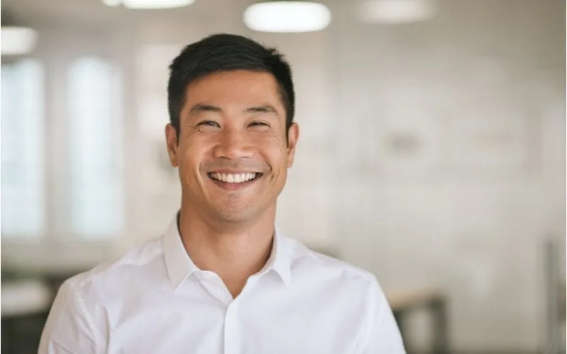 For a piece on asian men hairstyles, a well-dressed guy smiles at the camera in an office