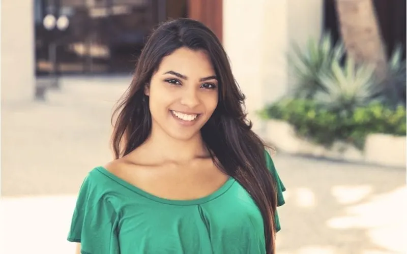 Young woman in a green blouse smiles at the camera and wears a Latina Hairstyle that is gorgeous
