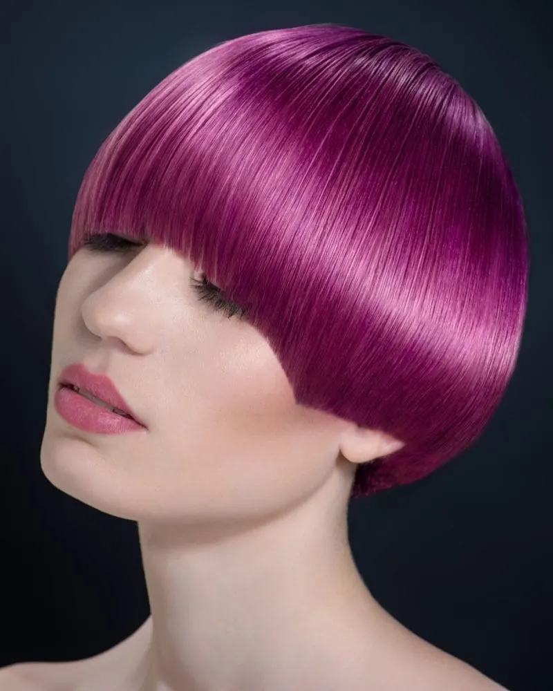 Woman with an arched fringe and pink hair that covers her eyebrows does not wear a shirt and looks down to the point her eyes are nearly closed
