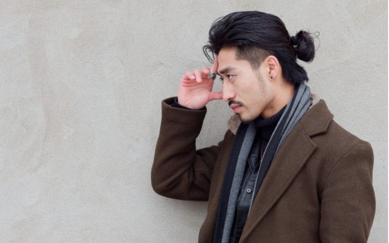 Side profile of an asian man with a faded man bun in a scarf and long jacket