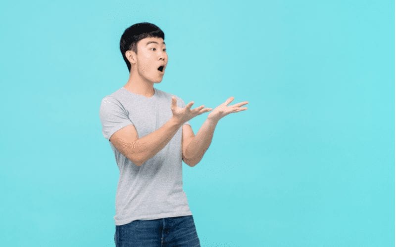 Young asian man holds his hands out and appears to be perplexed by something happening behind the camera