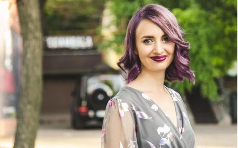 Woman with dark purple hair stands and looks at the camera in a dark floral and space themed shirt