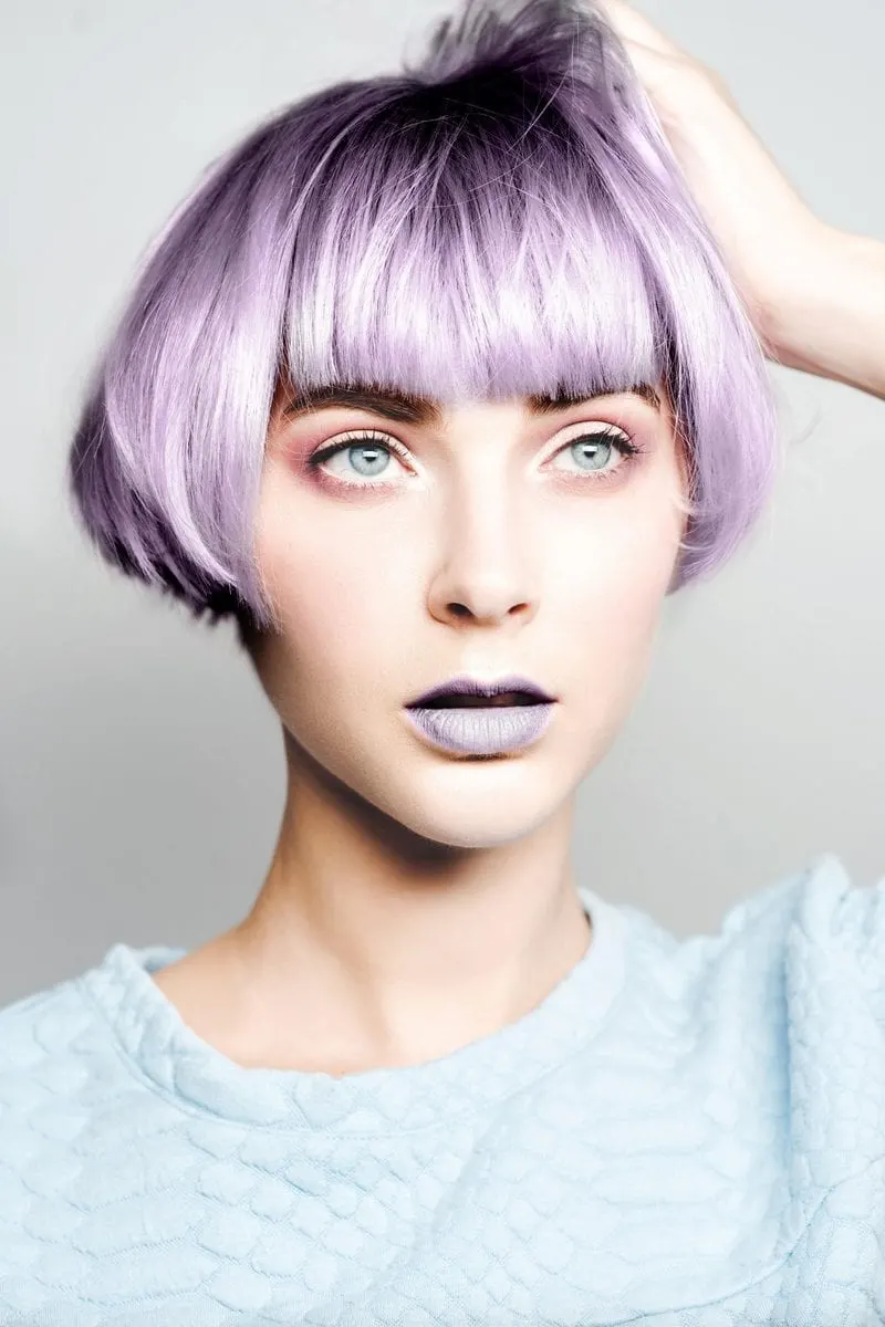 Woman with lilac hair stands with her hand on her head