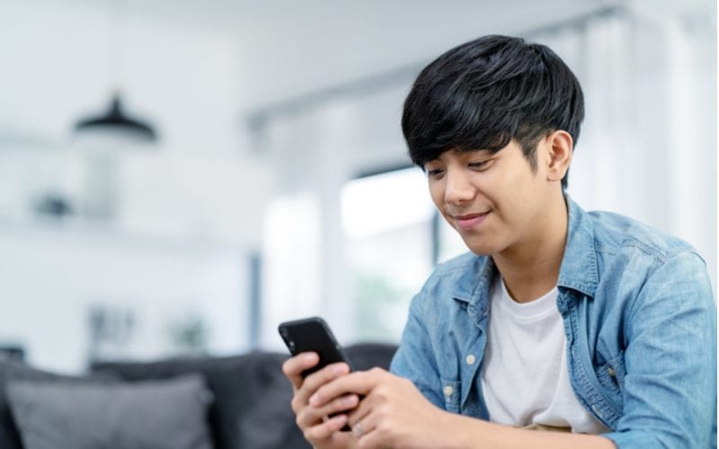 Happy asian teenager looking at a phone and wearing a popular asian man hairstyle popular among the youths