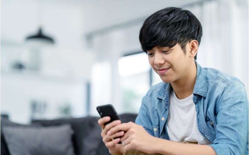 young asian man sitting inside and looking at his phone