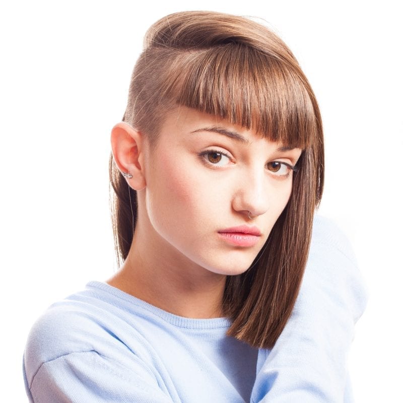 Woman with an undercut/bowl cut/shaved side holds her left shoulder