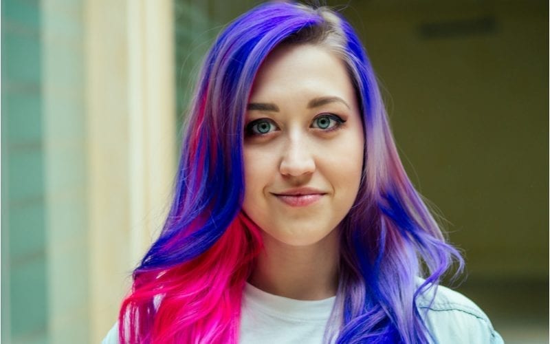 Woman with a purple and pink e-girl hairstyle stands outside