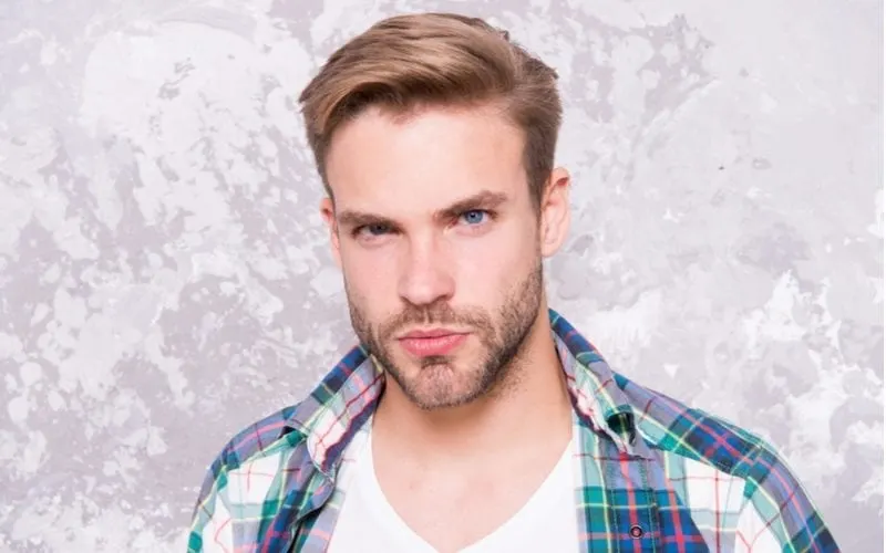Attractive man with a plaid shirt and a side-parted fade looks at the camera