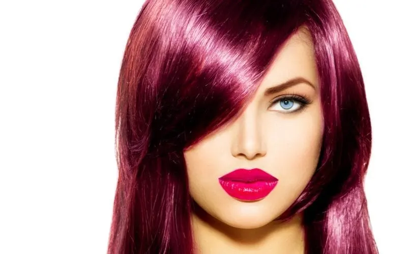 Gorgeous girl with piercing blue eyes and burgundy color hair and lipstick looks directly at the camera
