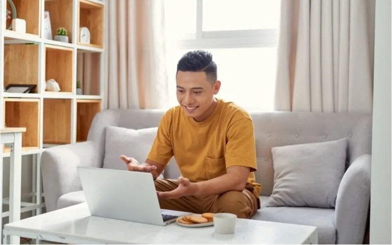 Man looking at a laptop and wondering what is going on on the screen while sitting in a modernly-decorated living room