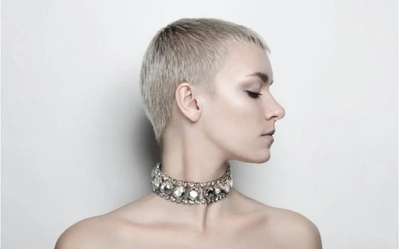 Elegant woman with a midi crop shaved hairstyle for women in a heavily jeweled necklace looks to the left