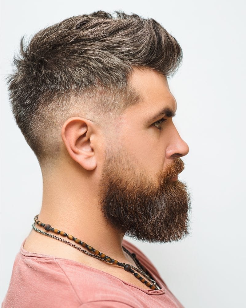 Side profile of a man with pooka shell necklace and a beard with a fade haircut