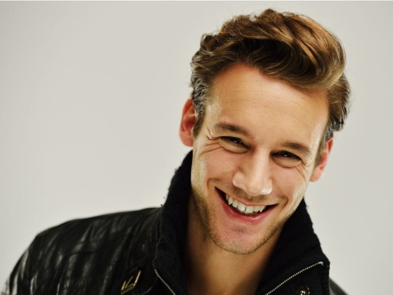 Man with a black leather jacket tilts his head to the left and smiles
