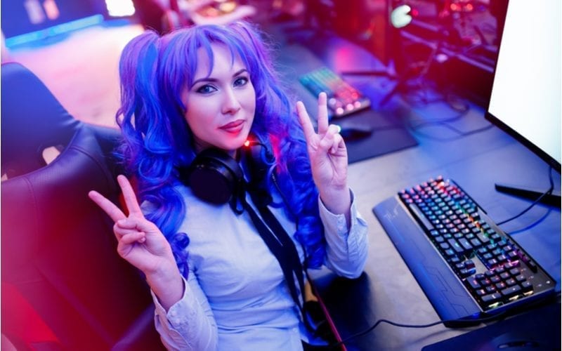Woman with blue e-girl hair gives 2 peace signs while sitting in front of a computer