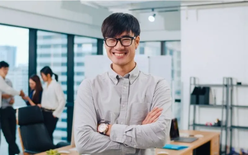 Asian man in glasses dressed in business casual attire in a high-rise office setting wearing a bowl cut with bangs combed to his right