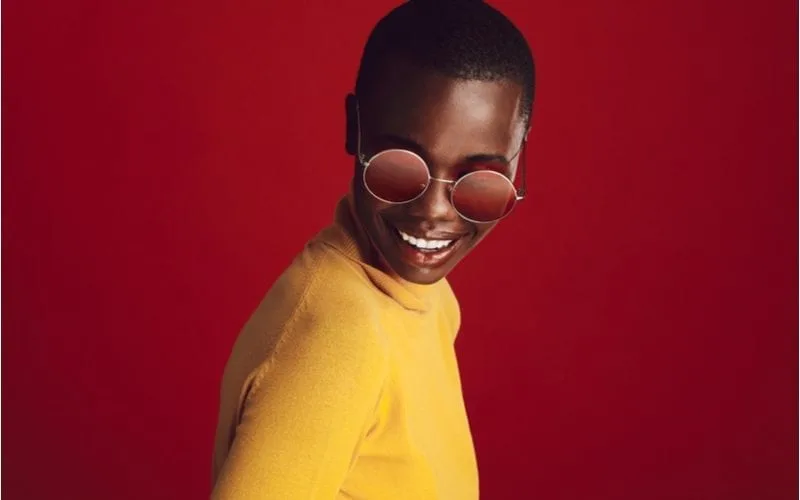 Pretty young african american model with round sunglasses standing against red background