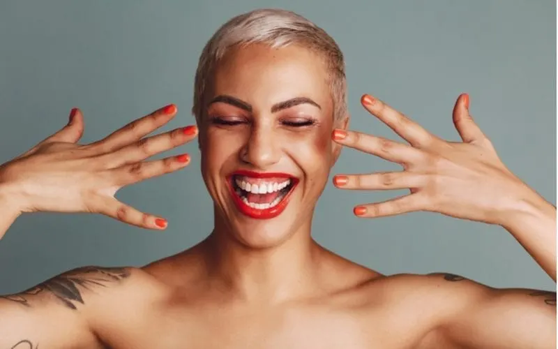 Excited woman with a shaved head pixie cut doing sideways jazz hands