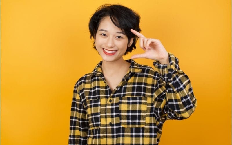 Short hair asian woman in a yellow and black flannel shirt holds up her hand and smiles