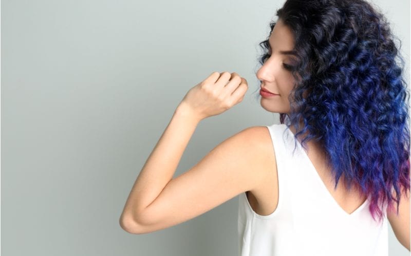 A woman with curly purple hair that fades to black holds her left hand up to her lip