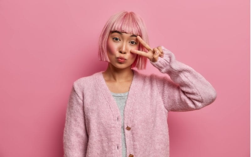 Asian short her woman with pink hair stands in front of a pink wall