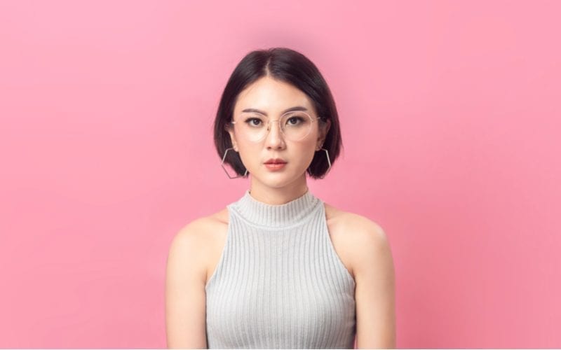 Against a pink background stands a woman with a cropped turtleneck stands in front of the camera