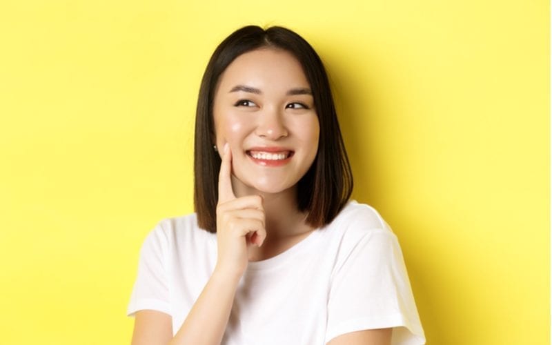 Radiant woman puts a finger to her chin and has a short asian haircut