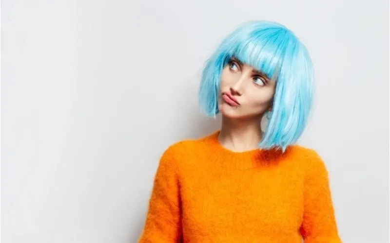 Person in a blue e-girl hairstyle wig looks up to the right with an orange sweater
