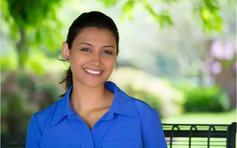 Woman with a bright blue button up shirt stands outside in a wooded area