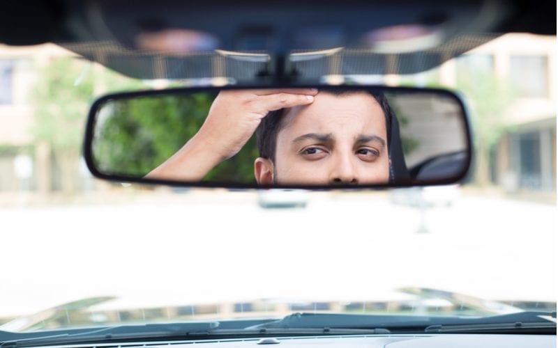 As an image for the best hairstyles for men with widows peaks, a guy looking at his receding hairline in the car mirror