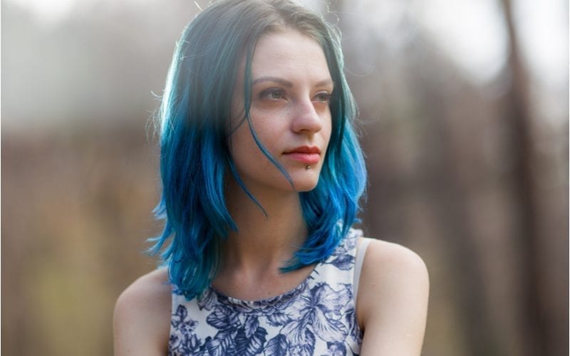 Young woman with dark hair that blends into blue roots wears a lip stud