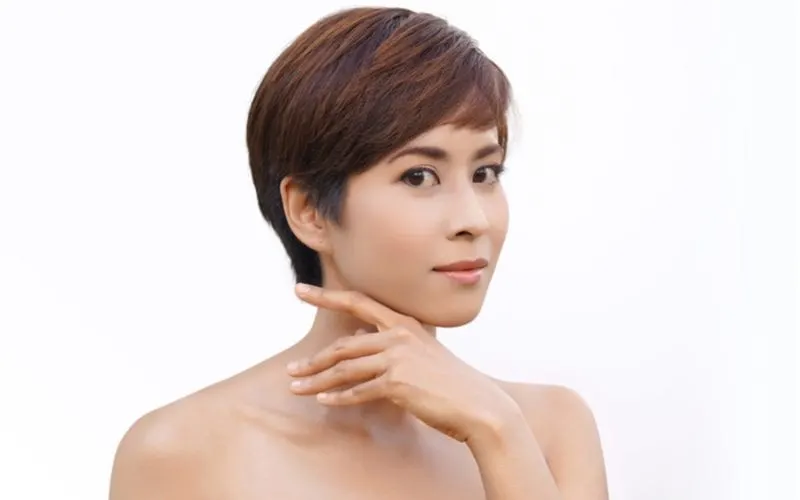 Asian short hair woman holds her hand up to her chin and does not smile while looking out of the corner of her eye