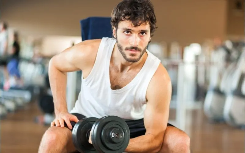 Man with a sporty shag haircut lifts weights in the gym and wears a tank top