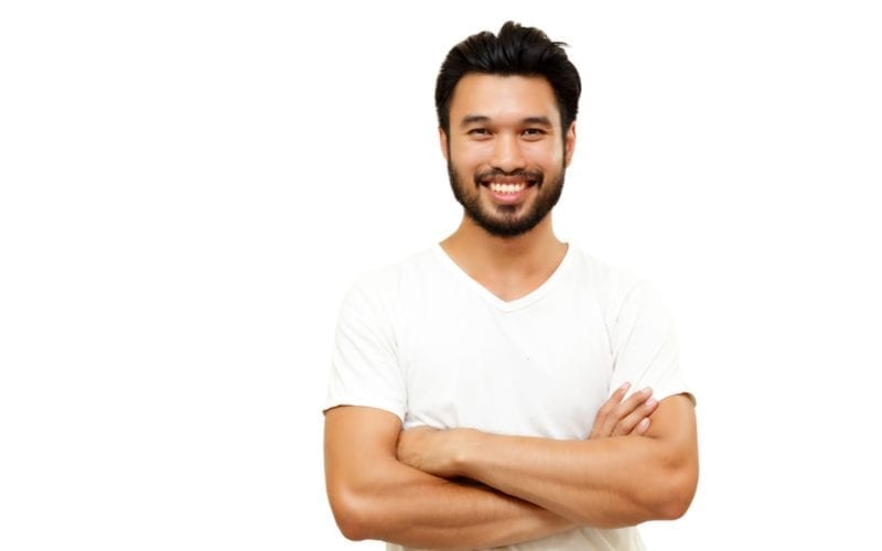 Asian man with an asian men hairstyle crossing his arms and smiling at the camera in a white v neck