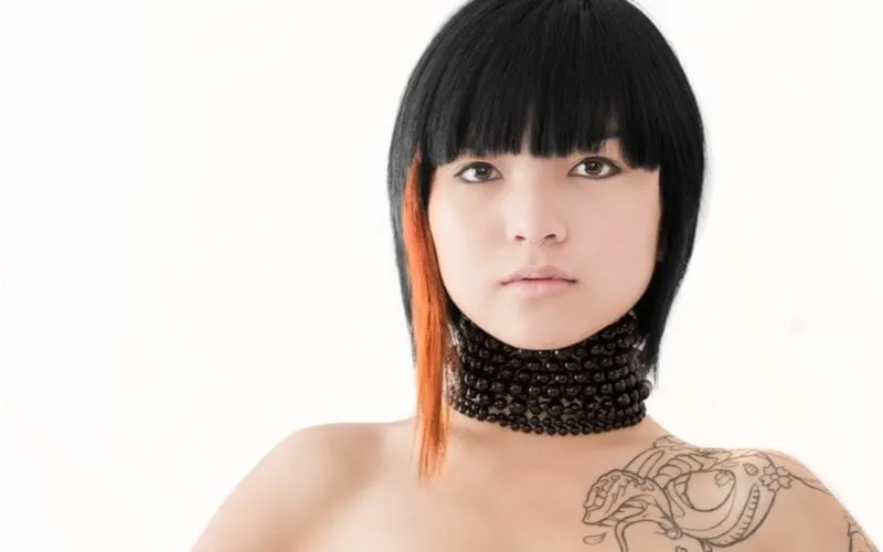 Very trendy asian woman with a short haircut wears a neck-long necklace and has a dragon tattoo