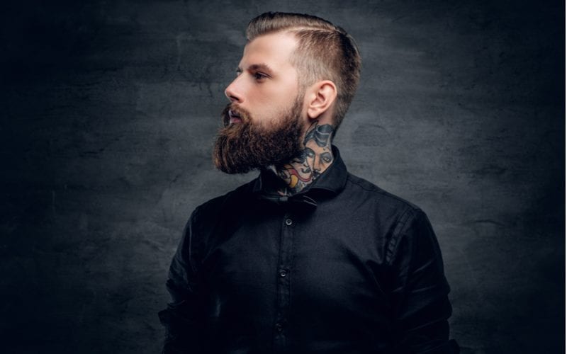 Man with a tattooed neck looks to the right with a gnarly beard and a taper fade haircut