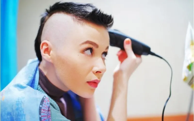 Woman with a half-shaved head shaves the other side with an electric razor