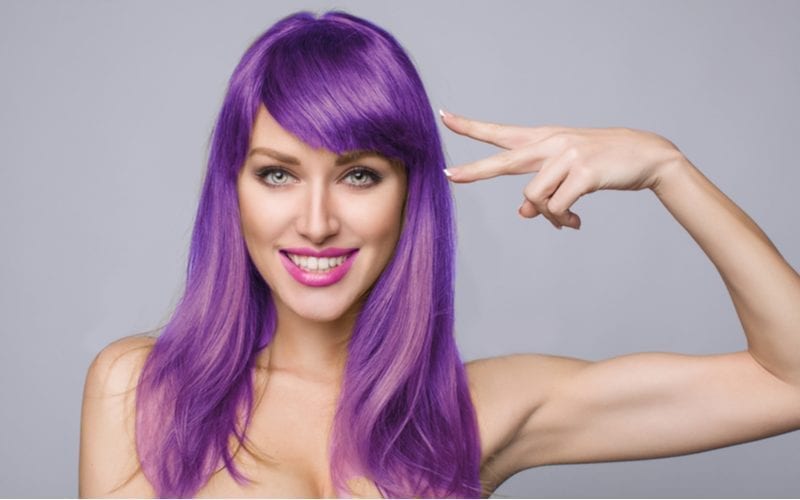 Attractive busty woman holds a sideways peace sign up to her purple hair
