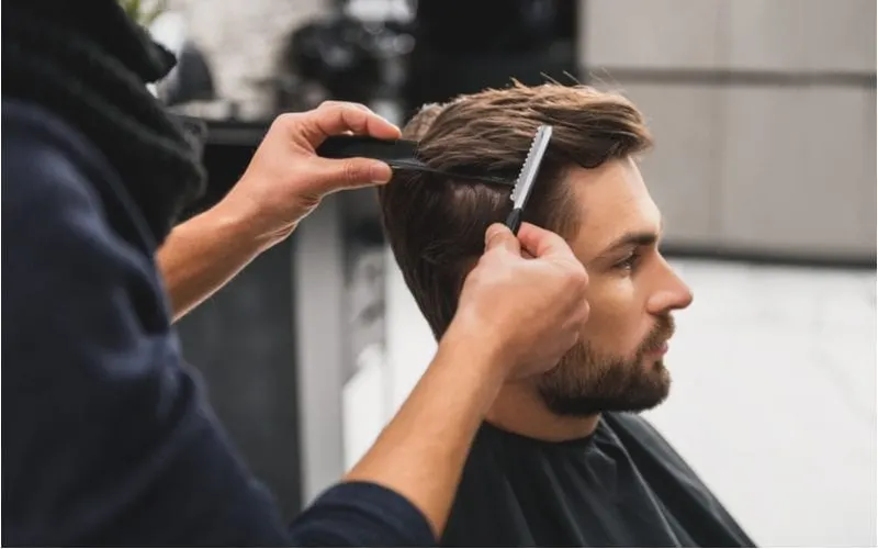 Man with a combed back taper sits in the barber shop for an image on a piece on haircuts for men with widows peak