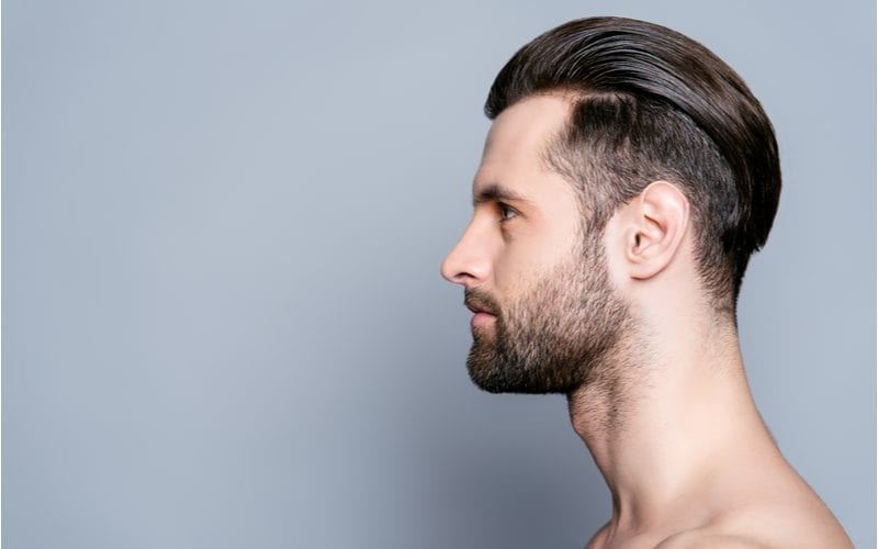 Side profile of a man with a combed-back tapered fade and a beard on a guy with no shirt