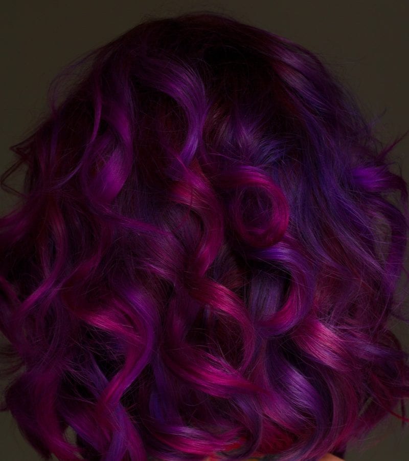 Beautiful model with purple hair stands against a dark brown background
