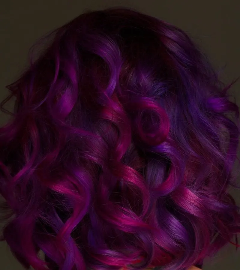 Beautiful model with purple hair stands against a dark brown background