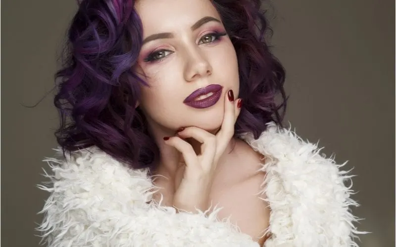 Vintage old hollywood style with a woman in a white feathered boa and purple hair and lipstick