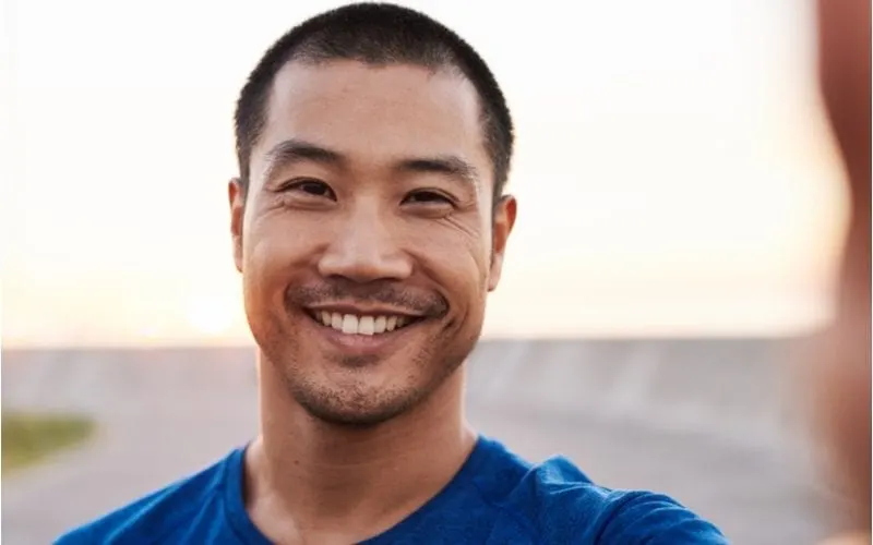 Young man smiles at the camera while standing on a beach and wearing a blue tshirt