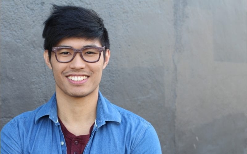For a feature on best haircuts for guys with big foreheads, a smiling asian man wearing a blue shirt