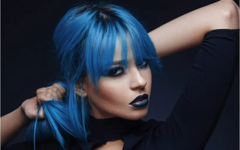 Attractive eastern-European woman with blue hair and dark blue lipstick looks at the camera and holds her ponytail