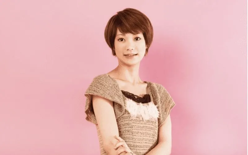 Asian short hair woman holds her right arm and stands in front of a pink wall