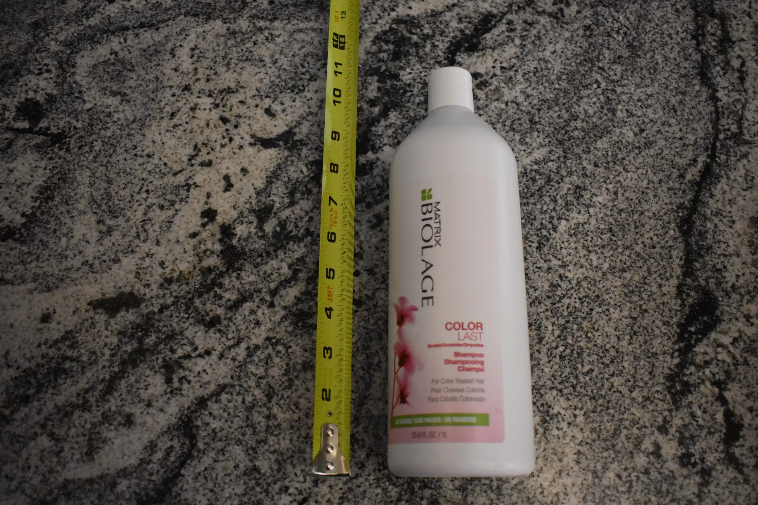 Biolage Colorlast shampoo sitting on a granite counter with a measuring tape next to it
