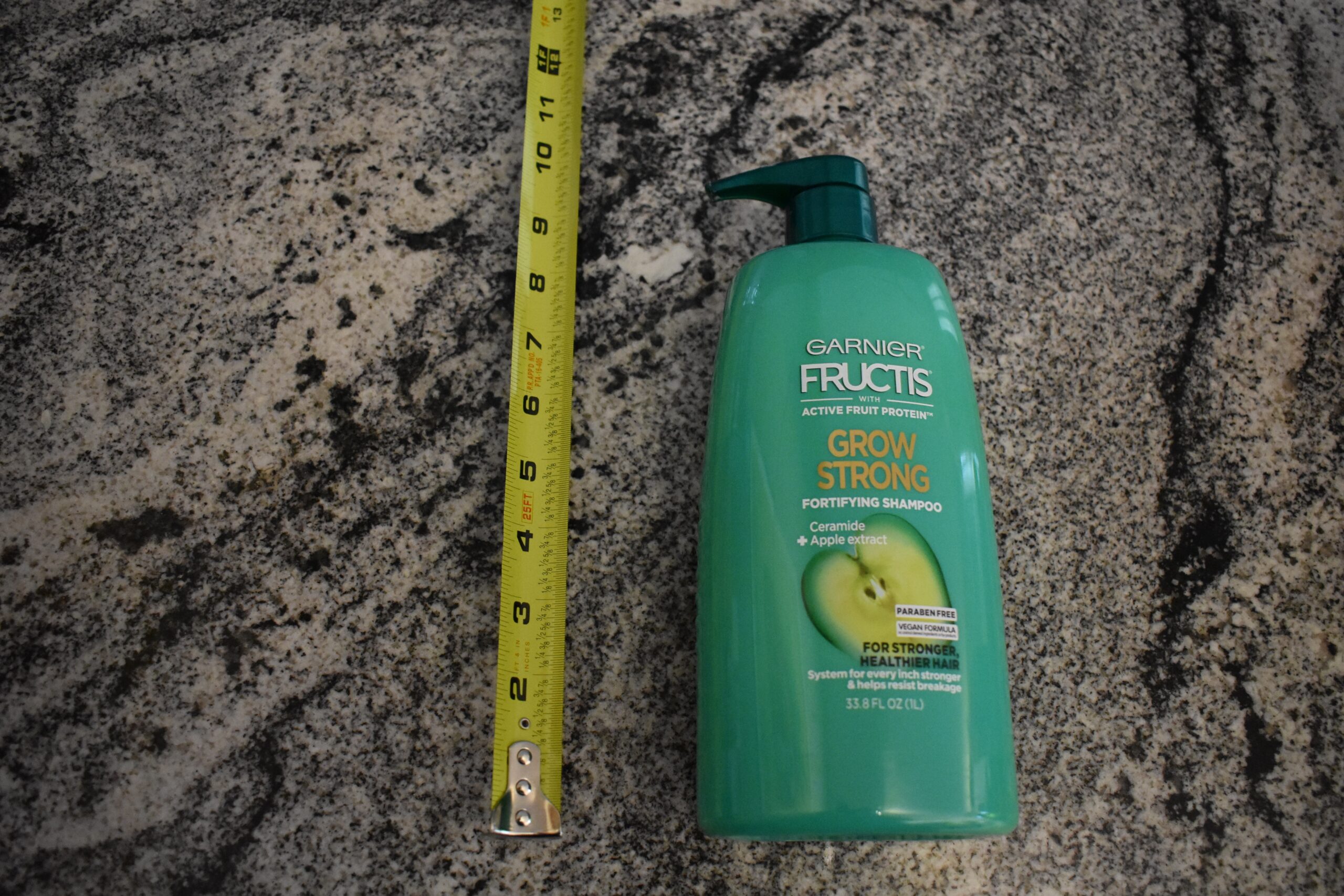 Garnier Fructis (best shampoo pick) on a grey granite counter sitting next to a measuring tape